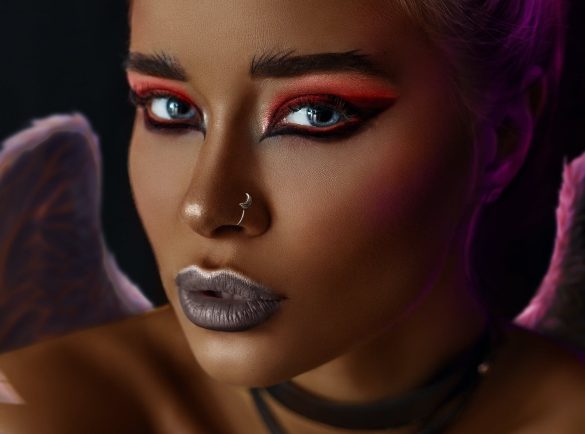 Beautiful female with stylish bright makeup and angel wings looking at camera against black background